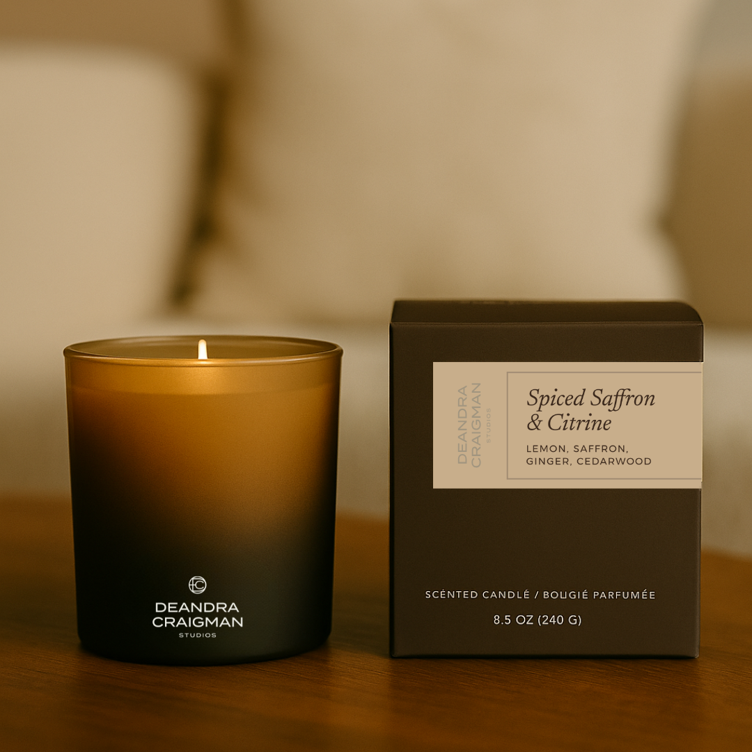 Deandra Craigman scented candle and packaging on a wooden surface with a blurred background