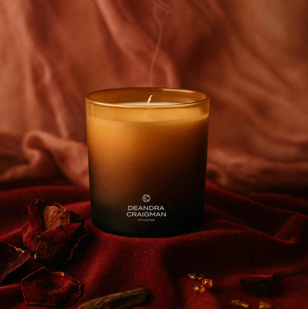 Candle with 'Deandra Craigman Studios' branding on a red fabric background