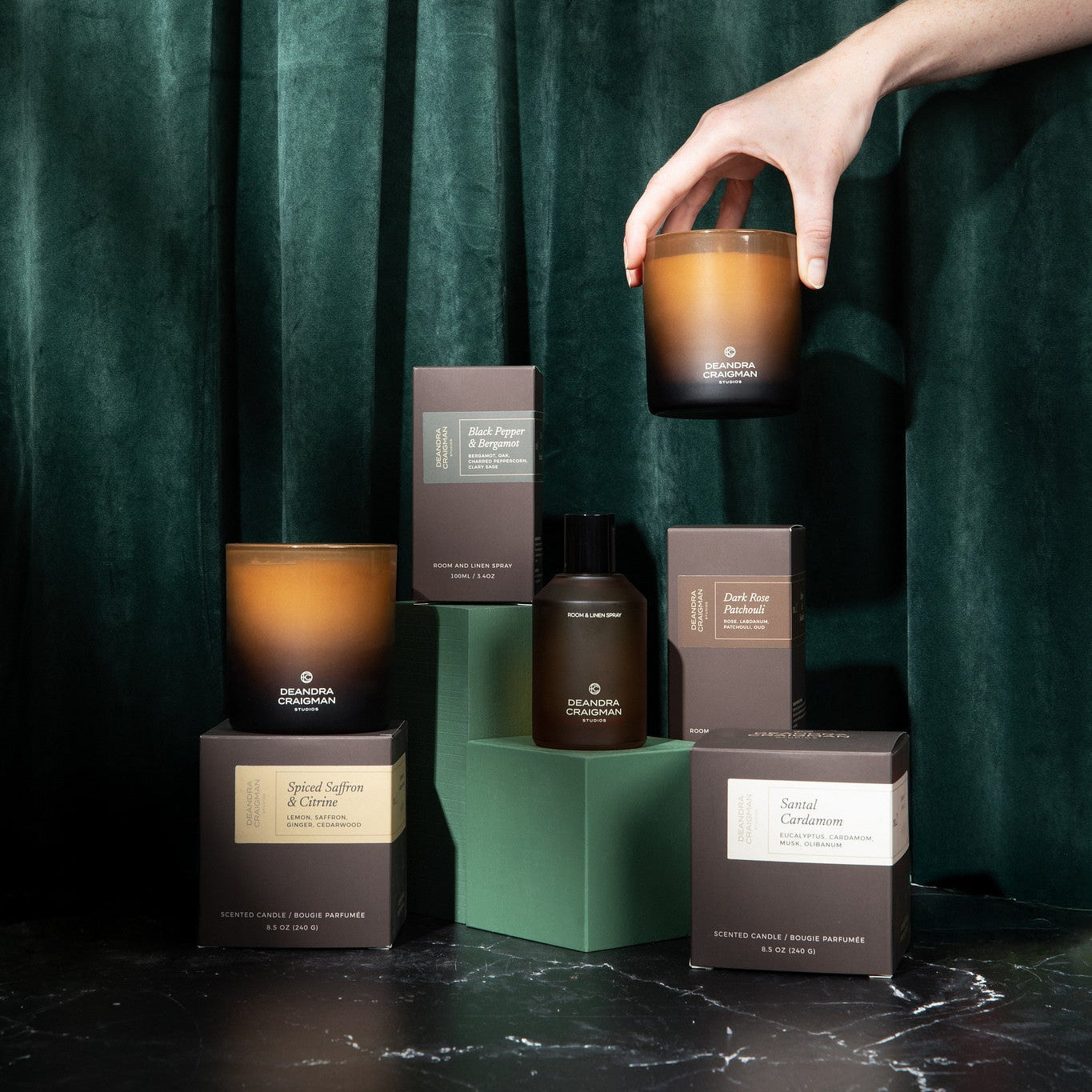 Candle and packaging set against a dark green curtain
