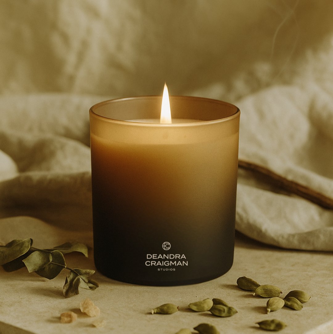 Candle with 'DeAndra Craigman Studios' branding on a neutral background